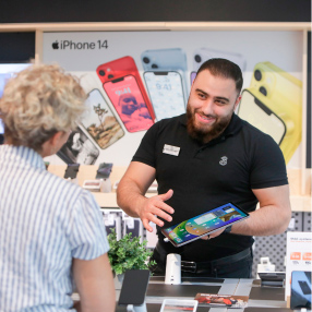 Smilende ekspedient viser tablet frem til kunde i butik