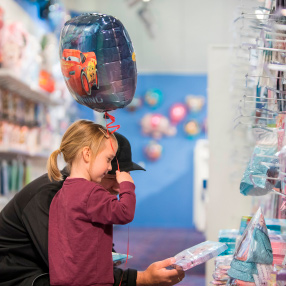 Far og datter der kigger på servietter. Datter har en ballon i hånden med biler på