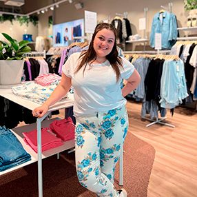 medarbejder står i butik iført hvide bukser med blå blomster