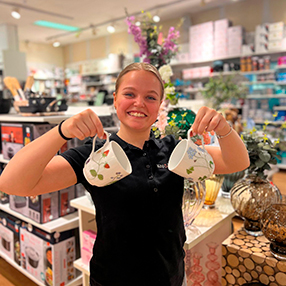 Ekspedient der holder to forskellige kopper op fra Kähler med blomsterprint fra Kop og Kande i Slagelse.