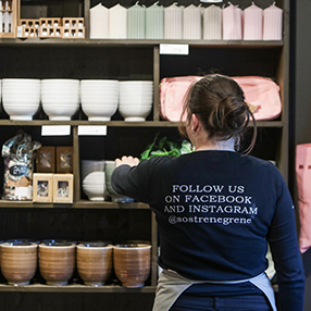 Ekspedient står ved hylder i butik og er i gang med at sætte op og gøre flot i butikken