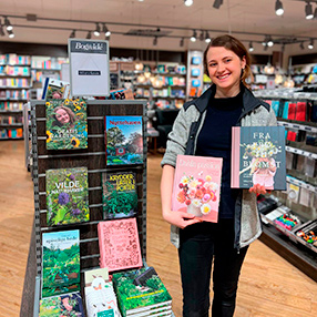 Medarbejder der fremviser to forskellige bøger fra Bog & idé i Slagelse der omhandler blomster.