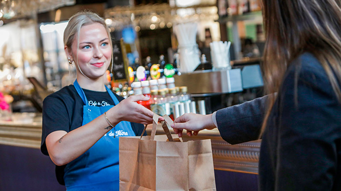 Medarbejder der rækker kunde pose med takeaway fra Café de Flore i Slagelse.